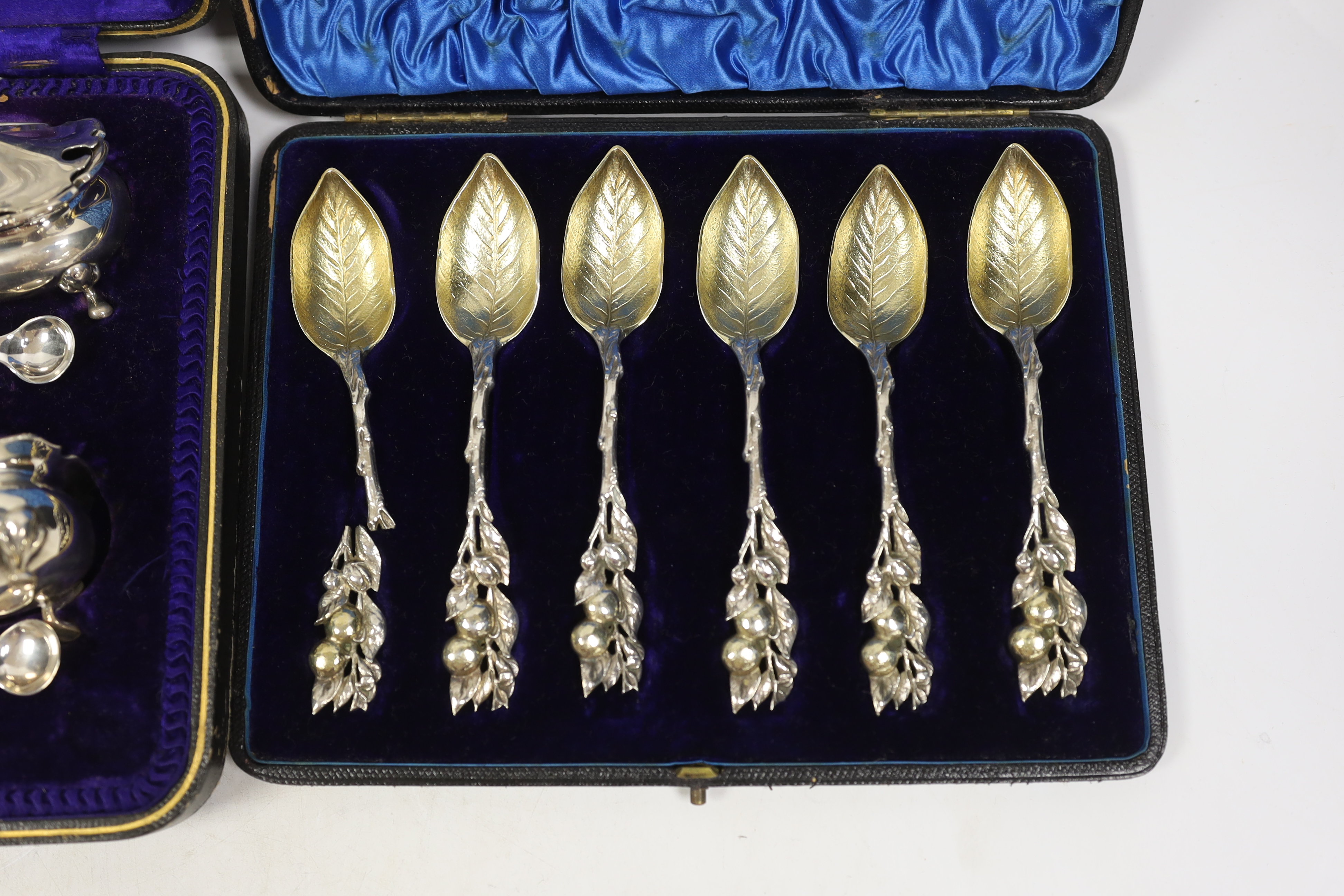 An Edwardian cased silver seven piece condiment set with four matching spoons, Hukin & Heath, Sheffield, 1908, together with an American cased set of parcel gilt sterling grapefruit spoons.